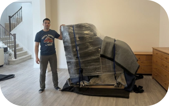 A Beaver Movers professional standing next to an upright piano expertly wrapped in moving blankets, shrink wrap, and heavy-duty straps for safe transport